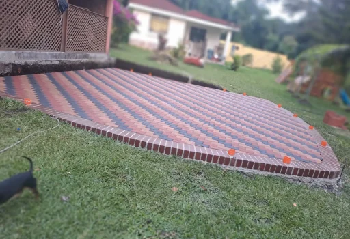 Instalación de adoquín decorativo para jardín en tonos rojo, negro y beige con remate de ladrillo perimetral.